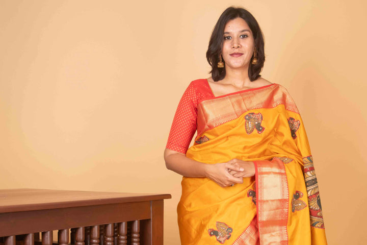 Woman wearing a yellow saree with a red blouse against a beige background